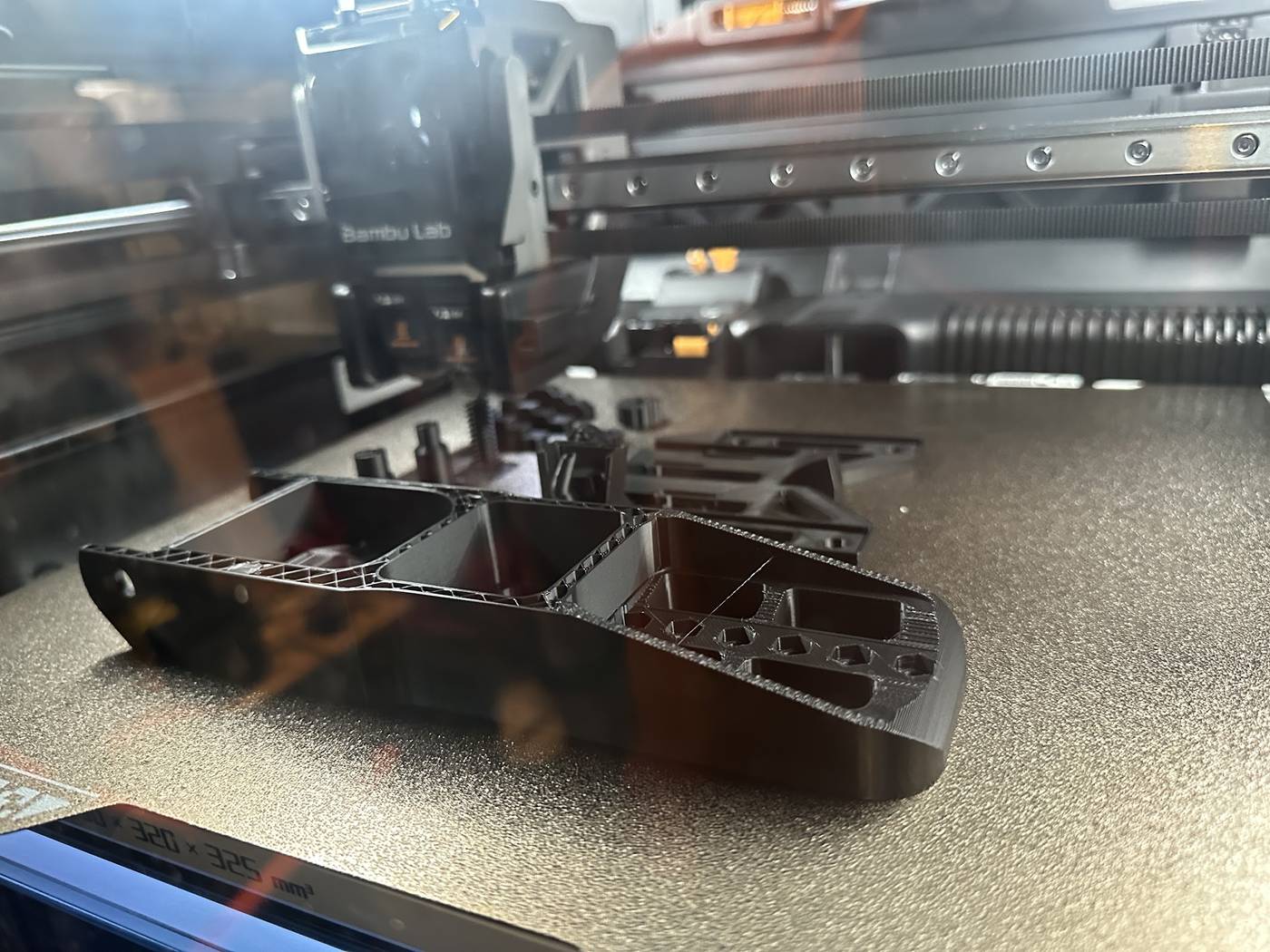 A structural bracket being 3D printed in-house, showing internal ribbing and lightening cut-outs.