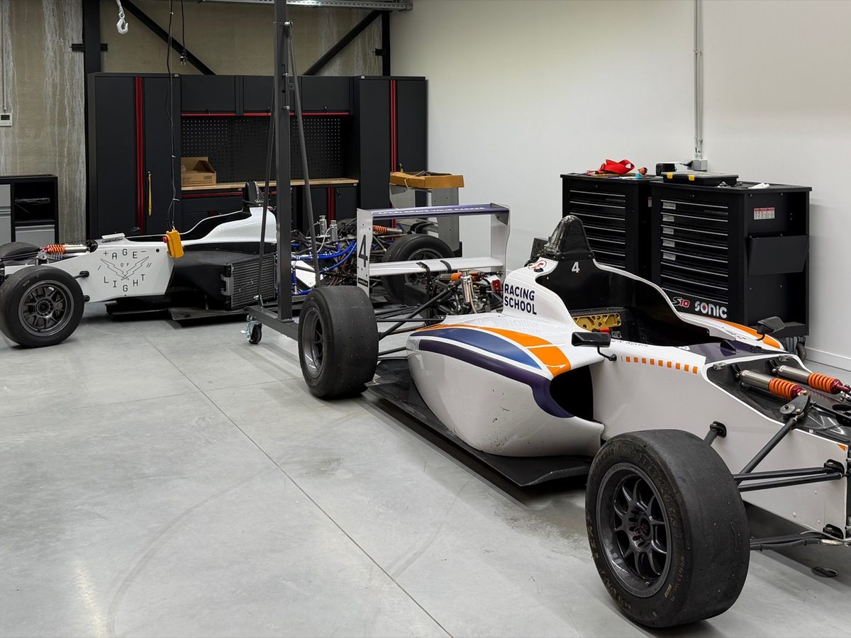 Two open-wheel racing school cars in the workshop, one with bodywork removed exposing its suspension.