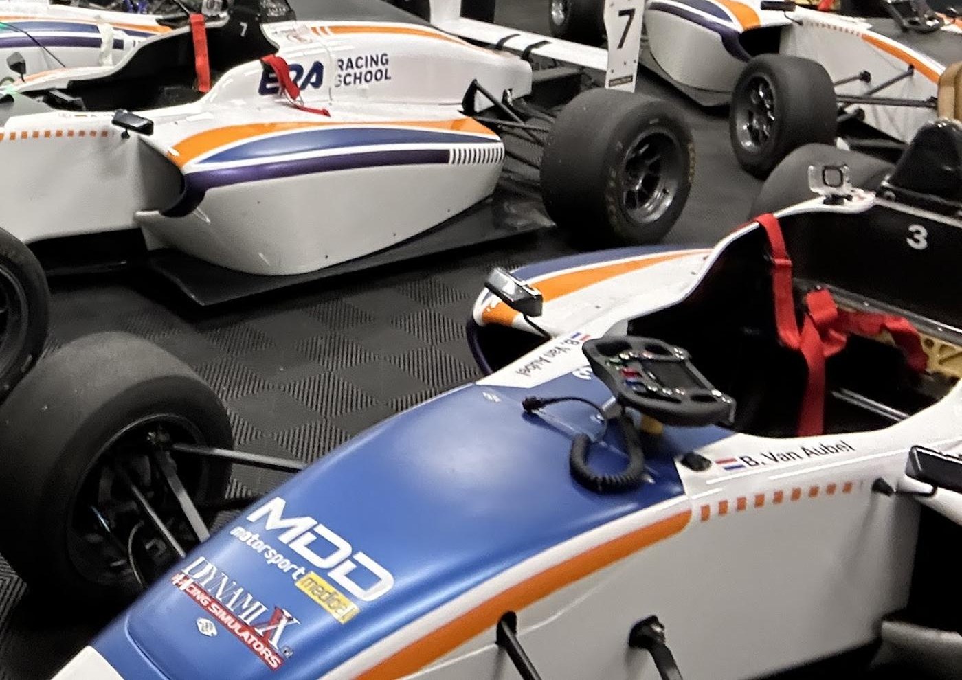 A fleet of electric formula cars in the team garage, with a cockpit and steering wheel in the foreground.