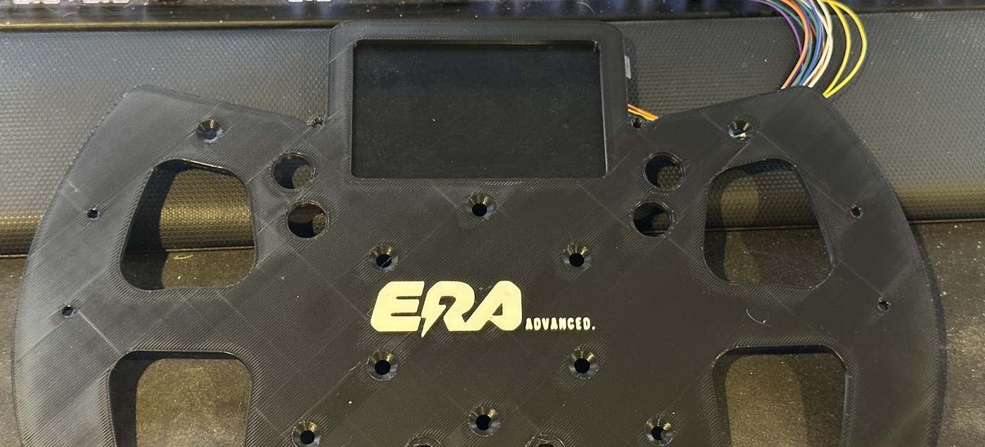 A 3D-printed steering wheel faceplate with display cut-out and wiring loom attached.
