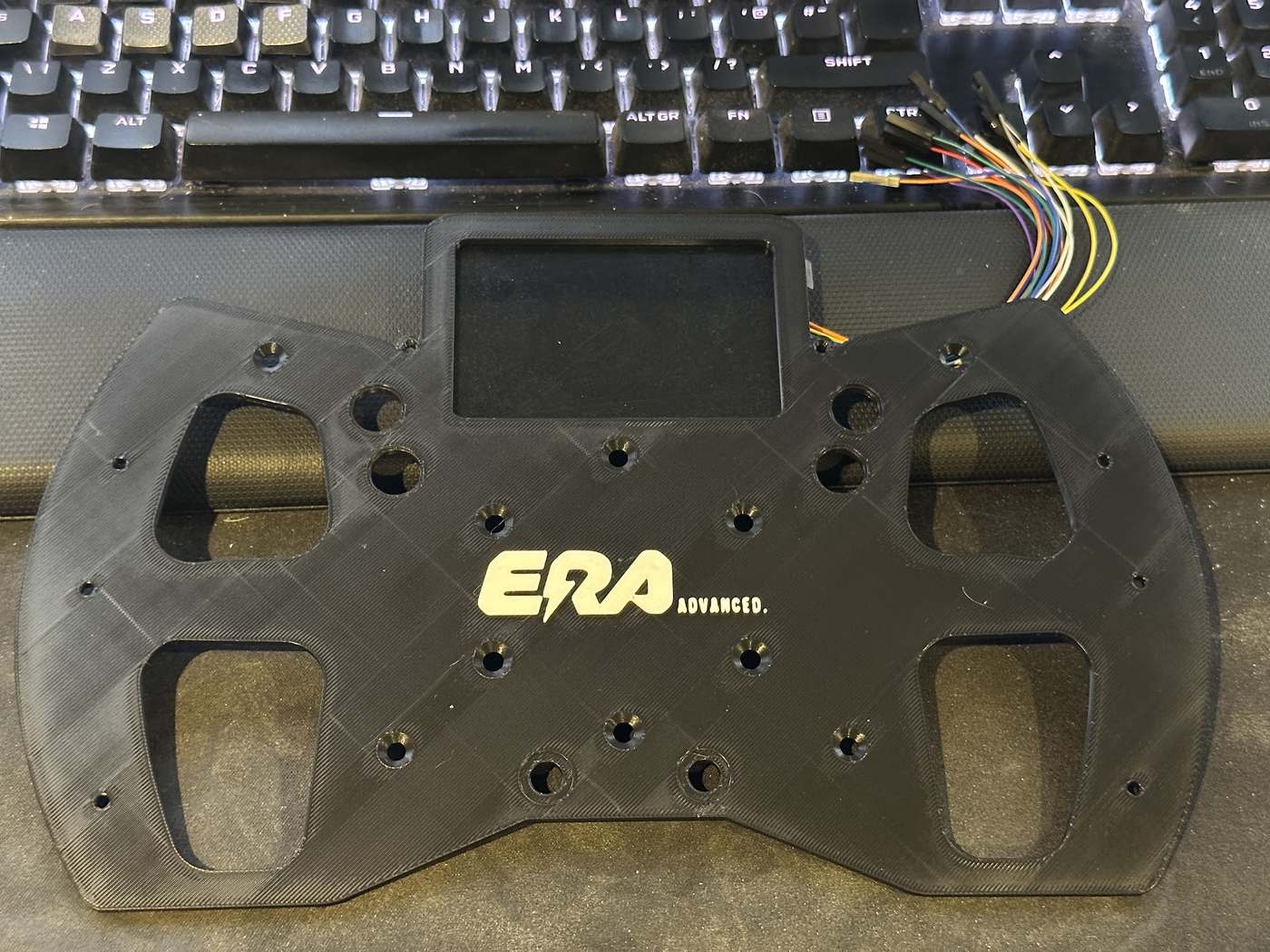 A 3D-printed steering wheel faceplate for an ERA Advanced formula car, with display cut-out and wiring loom attached.