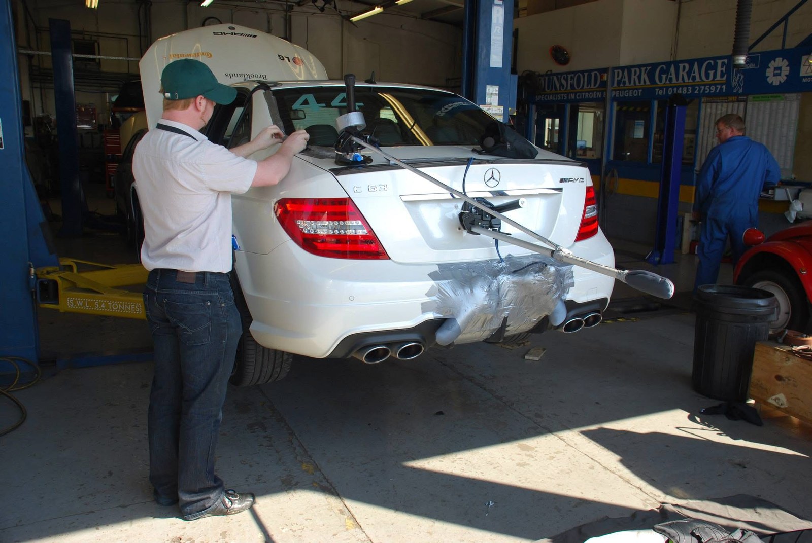A boom microphone braced against the rear bumper of a Mercedes C63 AMG in a workshop at Dunsfold.