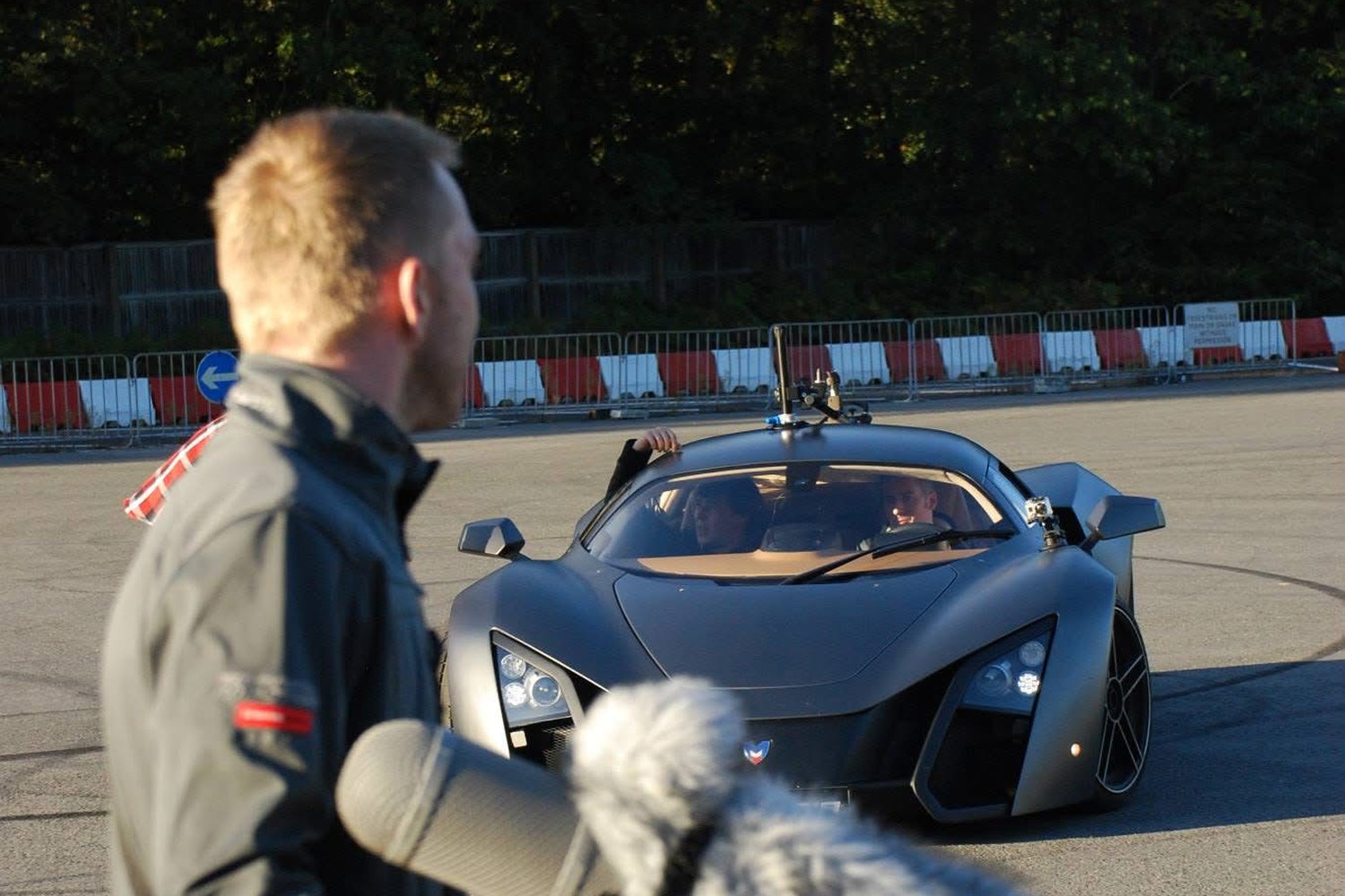 Holding a shotgun microphone in a windshield trackside as a Marussia supercar waits on the apron.