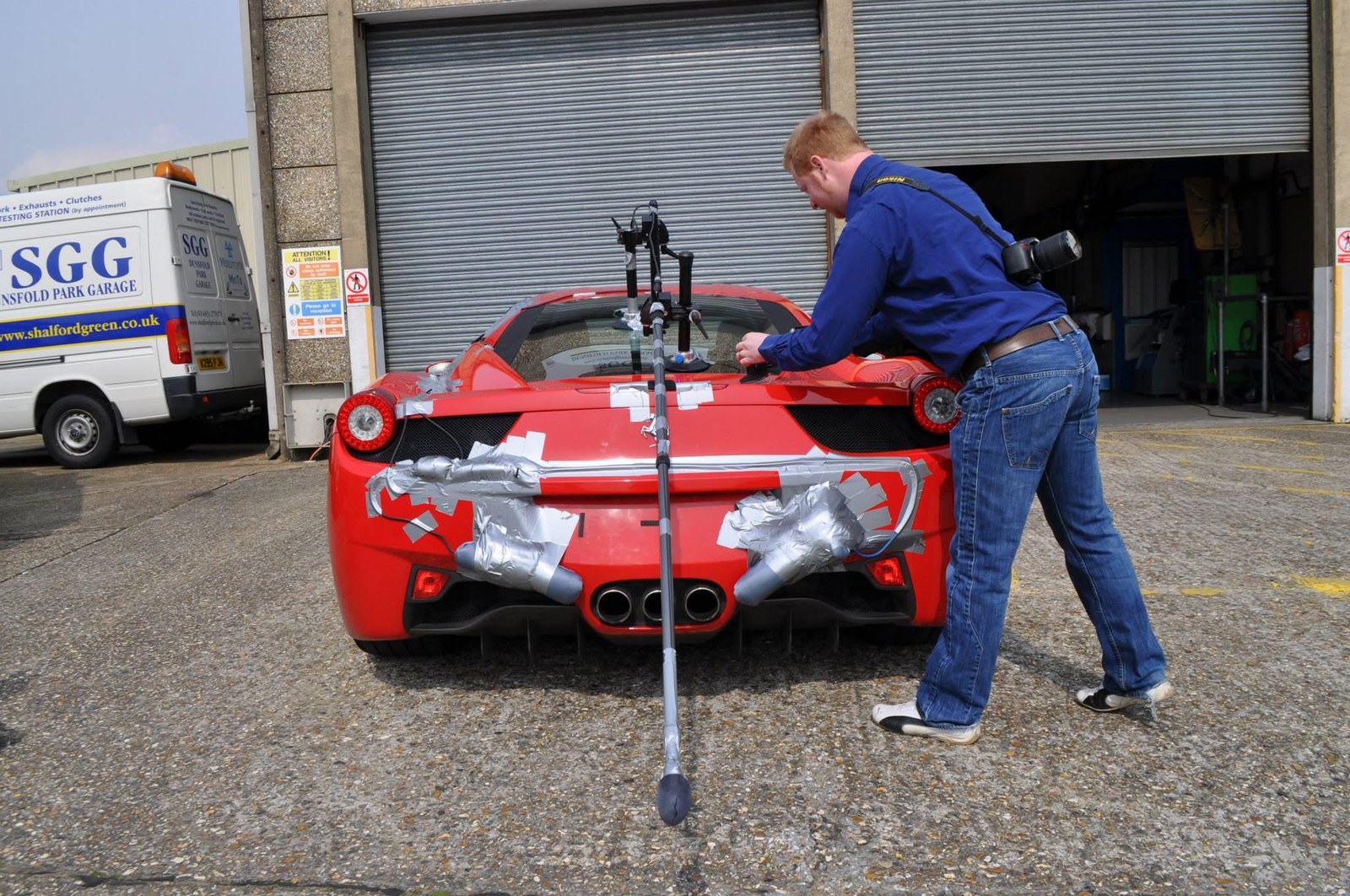 Microphones taped around the exhausts of a Ferrari 458 outside a garage, being rigged for audio capture.