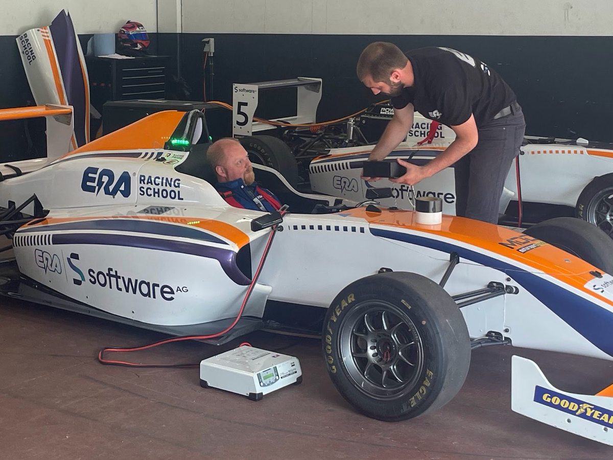 Oz in the cockpit of an ERA Racing School electric formula car while an engineer connects diagnostic equipment.
