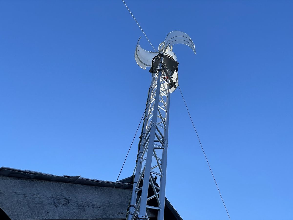 A small wind turbine on a guyed mast beside the building it powers.